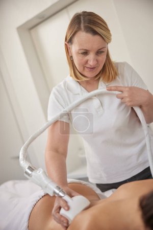 Photo for Problem areas, LPG massage, non-invasive method. Young woman in beauty salon doing beauty services, body shaping. Masseur is making vacuum roller massage for client, figure correction, anti cellulite - Royalty Free Image