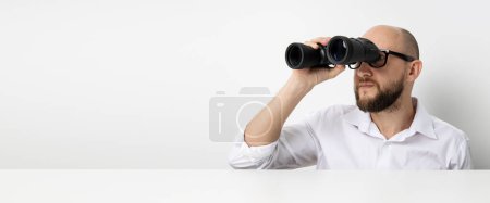 Young man looking through binoculars at table on white background. Banner.