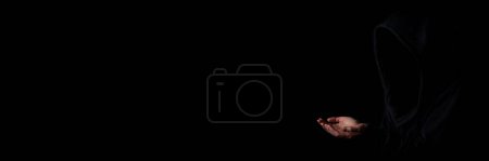 Photo for Young woman in black hood face not visible with palms outstretched against dark black background. Banner. - Royalty Free Image