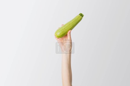 Photo for Female hand raised up fresh zucchini on a white background. - Royalty Free Image