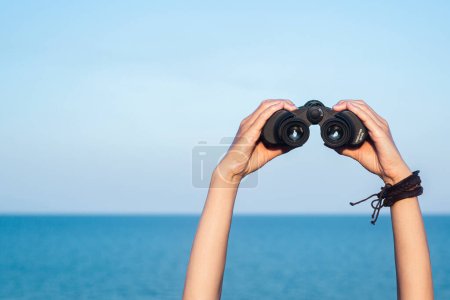 Photo for Female hands hold binoculars on the blue horizon, sky and sea background. - Royalty Free Image