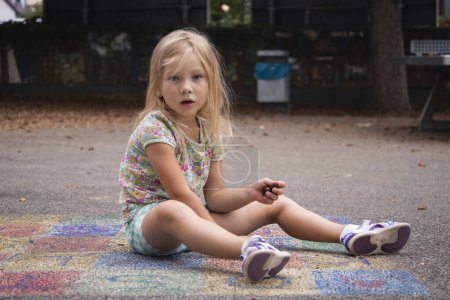 Photo for Child girl blonde preschool age is played sitting on the pavement. - Royalty Free Image