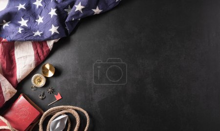 Happy Columbus Day concept. Vintage American flag, compass, paper boat, rope on dark stone background.  Flat lay, top view with copy space.