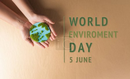 Hands holding paper earth with grass on brown background. World environment day, earth day and save earth concept.