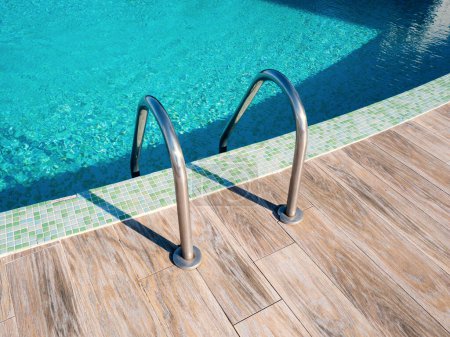 Téléchargez les photos : Escaliers à balustrades en acier dans la piscine avec eau bleue à l'hôtel close up. - en image libre de droit