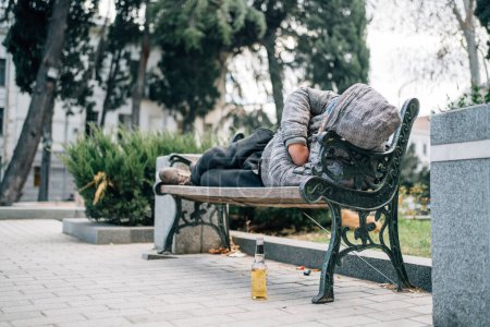 Foto de Homeless man sleeping on bench. Poor beggar on city street. - Imagen libre de derechos