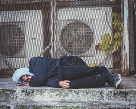 Homeless man sleeps on concrete steps in the city.