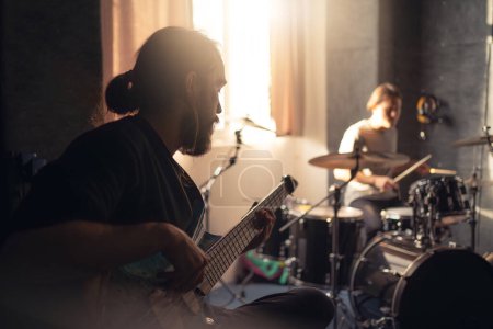 Band members practicing in a music studio with focus on guitarist.