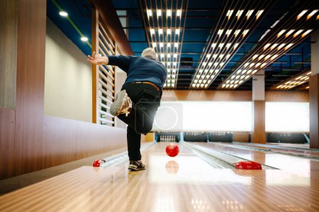 Senior man with throwing bowling ball, captured in modern bowling alley with vibrant lighting. 