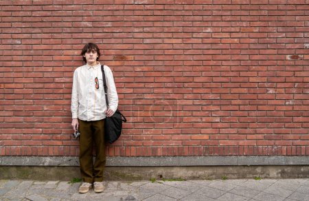 Young man photographer stands with vintage camera against red brick wall, copy space for text.
