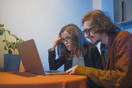 Couple collaborant sur le projet avec ordinateur portable, engageant avec le contenu. Le travail d'équipe et le concept de couple de pigistes.
