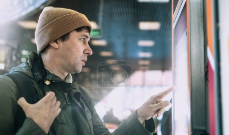 Mann interagiert mit Touchscreen in einem modernen urbanen Terminal. 