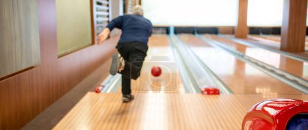 Homme âgé avec lancer boule de bowling, capturé dans une piste de bowling moderne avec un éclairage vibrant. 