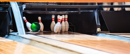 Bowling ball hits pins at end of glossy wooden bowling alley. 