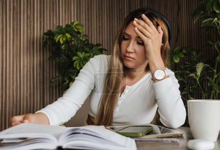 Stressed woman at work, holding head in frustration while reading documents. Workplace stress and mental strain. Work pressure, mental health, and professional challenges.