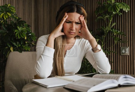 Frau empfindet Arbeitsstress, hält frustriert den Kopf, während sie von Dokumenten und Notizen umgeben ist. Beruflicher Druck und psychische Belastungen. Stress am Arbeitsplatz, psychische Gesundheit und Bürolebenskonzept.