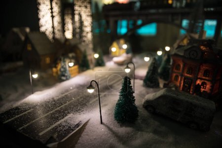 Foto de Pequeñas casas pequeñas decorativas en la nieve por la noche en invierno, Navidad y Año Nuevo casa en miniatura en la nieve por la noche con abeto. Concepto de vacaciones. Enfoque selectivo - Imagen libre de derechos