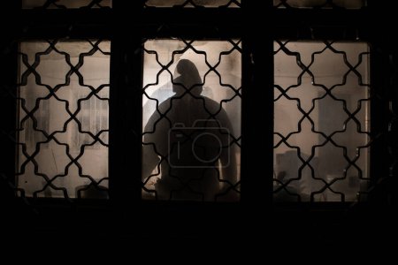 Foto de Silueta de una figura de sombra desconocida en una puerta a través de una puerta de cristal cerrada. La silueta de un humano frente a una ventana por la noche. Escena de miedo halloween concepto de silueta borrosa de maniaco. - Imagen libre de derechos