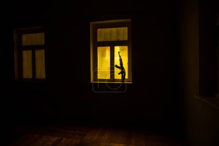 Photo for Conceptual photo of war between Russia and Ukraine. Russian weapon (rifle) on windowsill at night. Old creepy room with window. Explosion outside. - Royalty Free Image