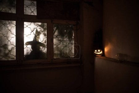Téléchargez les photos : Citrouille d'Halloween effrayant dans la fenêtre de la maison mystique la nuit ou citrouille d'Halloween et silhouette d'horreur dans la fenêtre. Concentration sélective - en image libre de droit