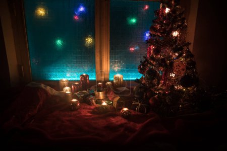 Foto de Navidad y Año Nuevo concept.Fir árbol de pie sobre alfombra roja con atributos tradicionales de vacaciones. Acogedora ventana con luces de colores en el fondo. Enfoque selectivo - Imagen libre de derechos