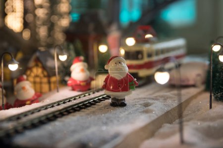 Téléchargez les photos : Miniature de scène hivernale avec maisons de Noël, gare, arbres, couverte de neige. Scène de nuit. Nouvel an dans la ville des jouets vintage. Concentration sélective - en image libre de droit