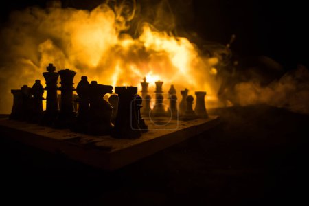 Téléchargez les photos : Chess board game concept of business ideas and competition or war theme. Chess figures on a dark background of explosion and fire clouds. Selective focus - en image libre de droit