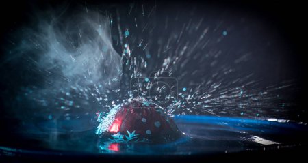 Photo for New year and Christmas concept. Glass bauble dropped into water or water splash on dark foggy background. Selective focus. - Royalty Free Image