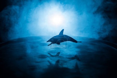 Photo for Abstract concept. Fish (shark) silhouette jumping on water at night. Water splash on dark foggy background. Selective focus. - Royalty Free Image