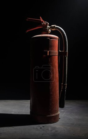Foto de Concepto de protección contra incendios. Antiguo extintor de incendios sobre fondo oscuro brumoso con luz. Enfoque selectivo - Imagen libre de derechos