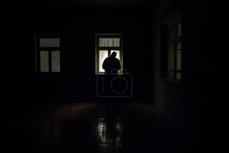 Photo for Conceptual photo of war between Russia and Ukraine. Silhouette of soldier at window at night. Old creepy room with window. Explosion outside. - Royalty Free Image