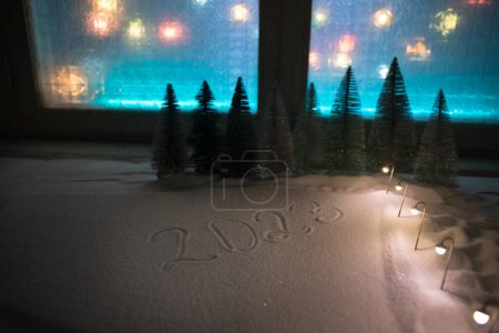 Foto de Casa en miniatura de Navidad y Año Nuevo en la nieve por la noche con abeto. Pequeña casa de juguete en la nieve con el árbol y las luces de la ciudad bokeh en el fondo. Decoraciones navideñas. Enfoque selectivo - Imagen libre de derechos