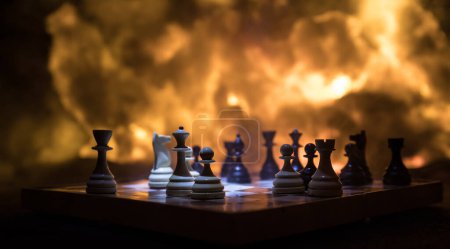 Foto de Chess board game concept of business ideas and competition or war theme. Chess figures on a dark background of explosion and fire clouds. Selective focus - Imagen libre de derechos
