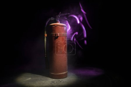 Photo for Fire protection concept. Old fire extinguisher on dark foggy background with light. Selective focus - Royalty Free Image