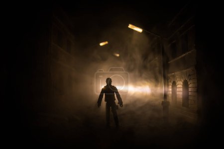 Foto de Triste hombre solo caminando por el callejón en el parque de niebla nocturna. Ciudad arruinada decorativa. Enfoque selectivo - Imagen libre de derechos