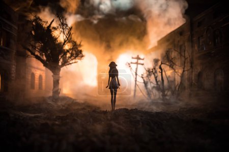 Photo for Artwork decoration. Woman standing on a road of burnt up city. Apocalyptic view of city downtown as disaster film poster concept. Night scene. City destroyed by war. Selective focus - Royalty Free Image