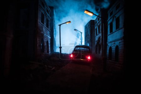 Téléchargez les photos : Silhouette of old vintage car in dark foggy abandoned city with glowing lights, or silhouette of old crime car dark background. Selective focus - en image libre de droit