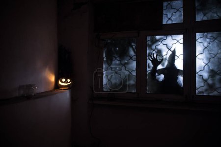 Téléchargez les photos : Citrouille d'Halloween effrayant dans la fenêtre de la maison mystique la nuit ou citrouille d'Halloween et silhouette d'horreur dans la fenêtre. Concentration sélective - en image libre de droit