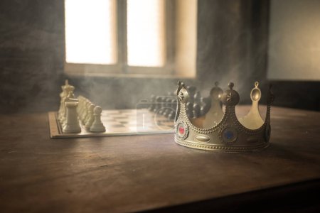 Photo for Beautiful crown miniature on chessboard. chess board game concept of business ideas. Chess figures on a dark background with smoke and fog. Selective focus - Royalty Free Image