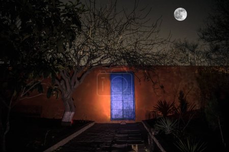 Foto de Luna llena sobre pueblo tranquilo por la noche. Pared naranja con puerta metálica azul por la noche. Atmósfera de horror embrujada. Disparo de larga exposición - Imagen libre de derechos