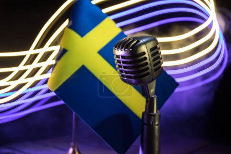Téléchargez les photos : Microphone sur fond de drapeau flou Suède gros plan. décoration de table sombre. Concentration sélective - en image libre de droit