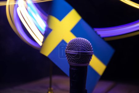 Foto de Micrófono en un fondo de una bandera borrosa Suecia primer plano. decoración de mesa oscura. Enfoque selectivo - Imagen libre de derechos