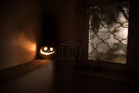 Téléchargez les photos : Citrouille d'Halloween effrayant dans la fenêtre de la maison mystique la nuit ou citrouille d'Halloween la nuit sur la chambre abandonnée avec fenêtre. Concentration sélective - en image libre de droit
