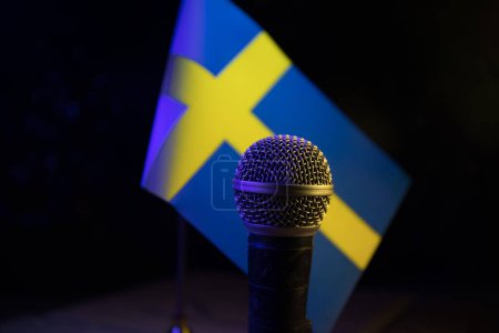 Foto de Micrófono en un fondo de una bandera borrosa Suecia primer plano. decoración de mesa oscura. Enfoque selectivo - Imagen libre de derechos