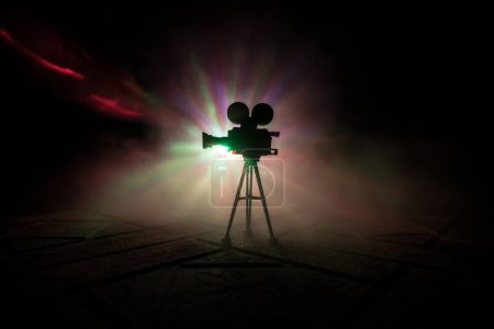 Photo for Movie concept. Miniature movie set on dark toned background with fog and empty space. Silhouette of vintage camera on tripod. Selective focus - Royalty Free Image