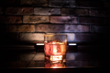 Foto de Concepto de bebida de whisky. Vaso de whisky y hielo con luz de color y niebla sobre fondo de barra oscura. Enfoque selectivo - Imagen libre de derechos