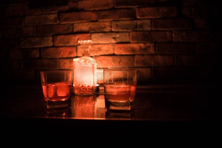 Photo for Whiskey drink concept. Glass of whiskey and ice with color light and fog on dark bar background. Selective focus - Royalty Free Image