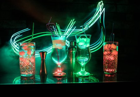 Foto de Cóctel colorido en vidrio sobre fondo oscuro o vasos de cócteles en el fondo del bar.Club de fiesta de entretenimiento. Luz mixta - Imagen libre de derechos