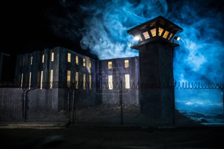 Criminal justice imprisonment concept. Old prison watchtower protected by wire of prison fence at night. Creative art decoration. Selective focus