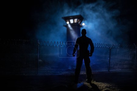 Photo for Criminal justice imprisonment concept or prison break concept. Silhoette of prisoner standing near of prison fence with watchtower at night. Creative art decoration. Selective focus - Royalty Free Image